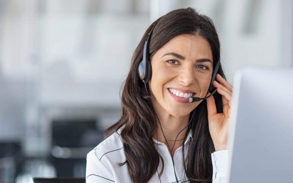 Na imagem, vê-se uma atendente de call center sorrindo, simbolizando a melhoria do TMA (Tempo Médio de Atendimento) devido a um atendimento eficiente.