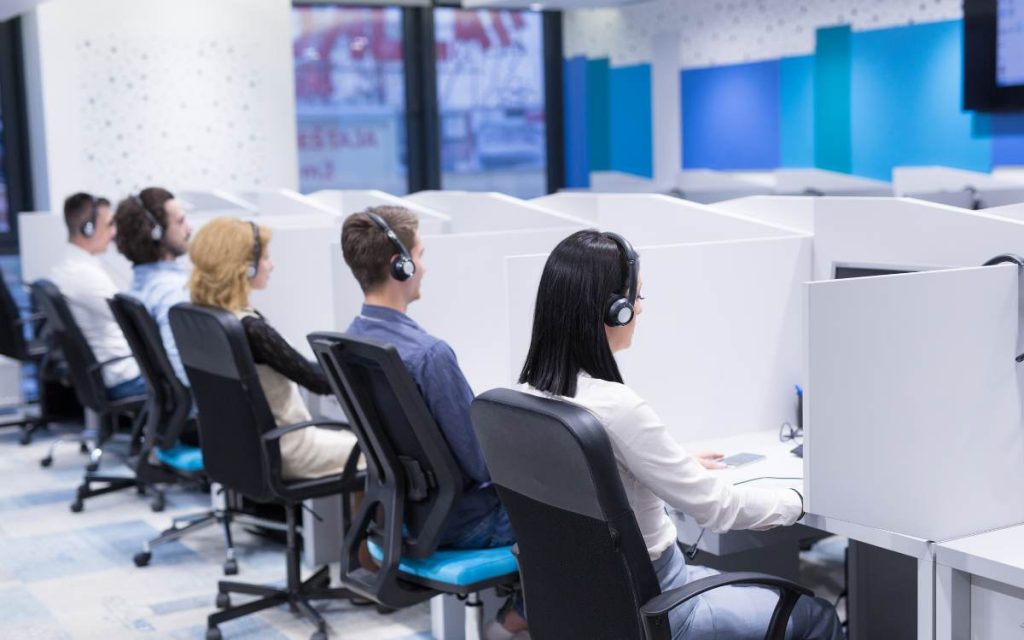 Na imagem, uma equipe de call center trabalha em suas estações, representando a eficiência e a melhoria do TMA (Tempo Médio de Atendimento) através de processos otimizados.